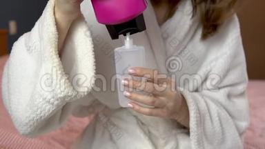 一个女人把洗发水倒进一个小罐子里。 穿浴袍的女人拿着一罐旅行洗发水